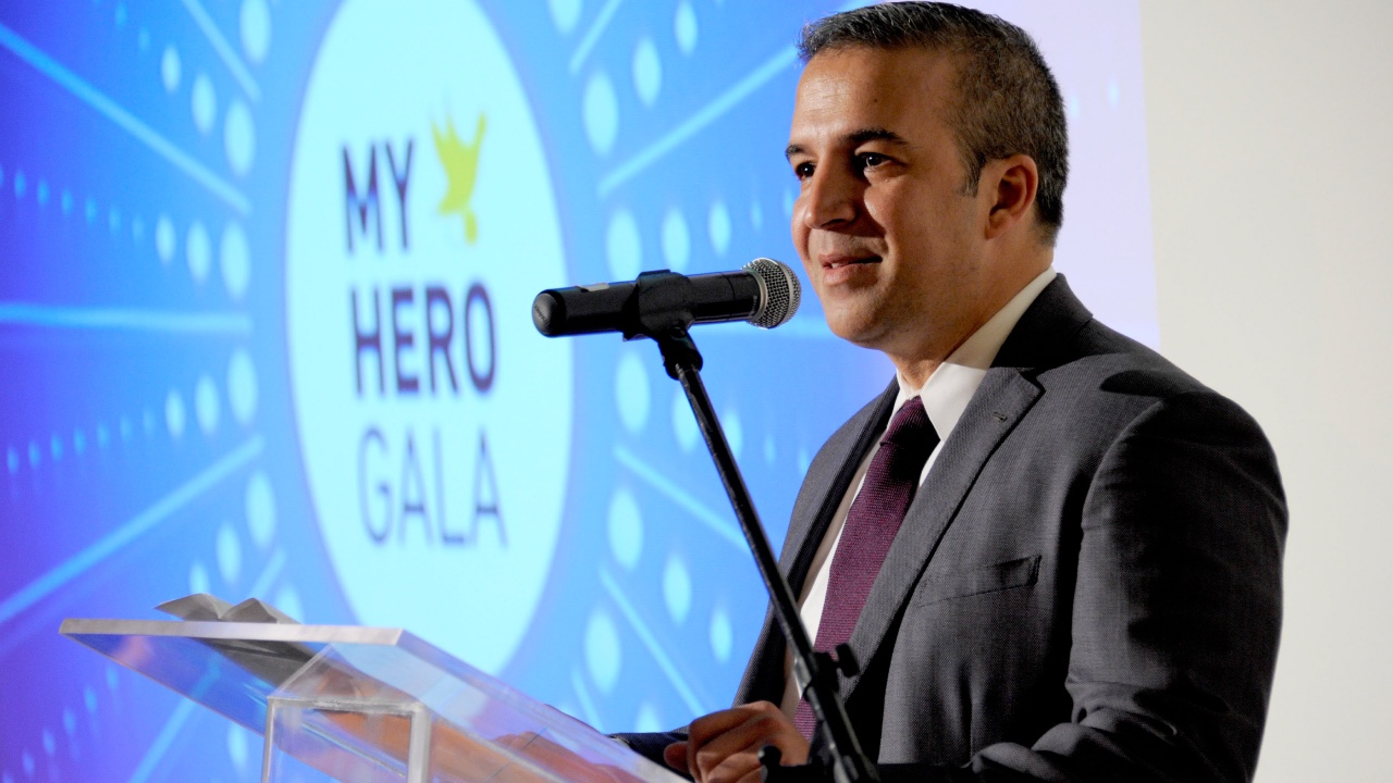 A man in a suit standing at a podium during the My Hero Gala.