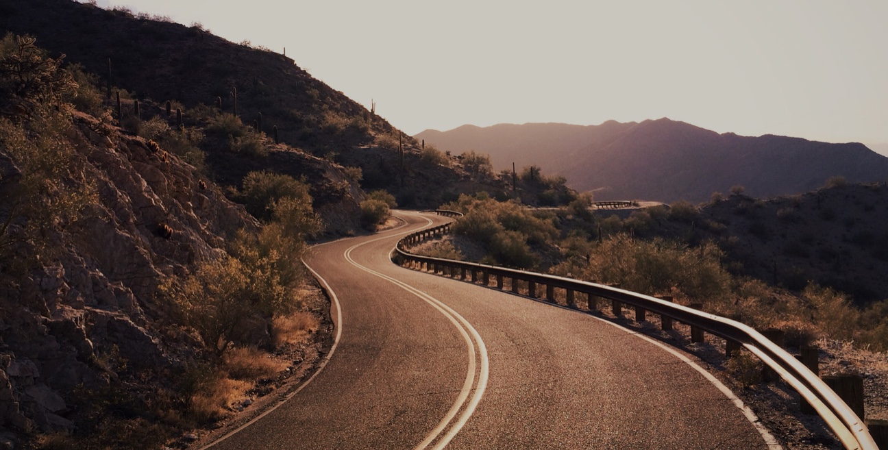 A winding road in the desert with mountains in the background.