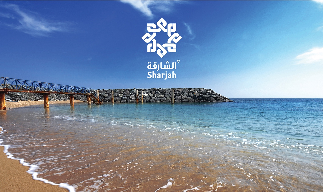 A beach with a pier and the logo of The Sharjah Commerce and Tourism Development Authority (SCTDA)