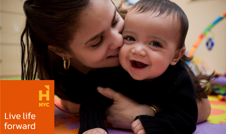 A woman kisses a baby on the floor.