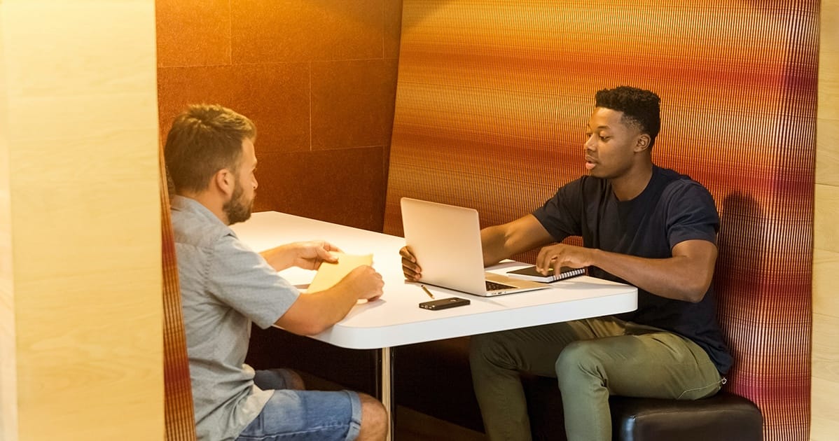 Two men sitting at a table with laptops.