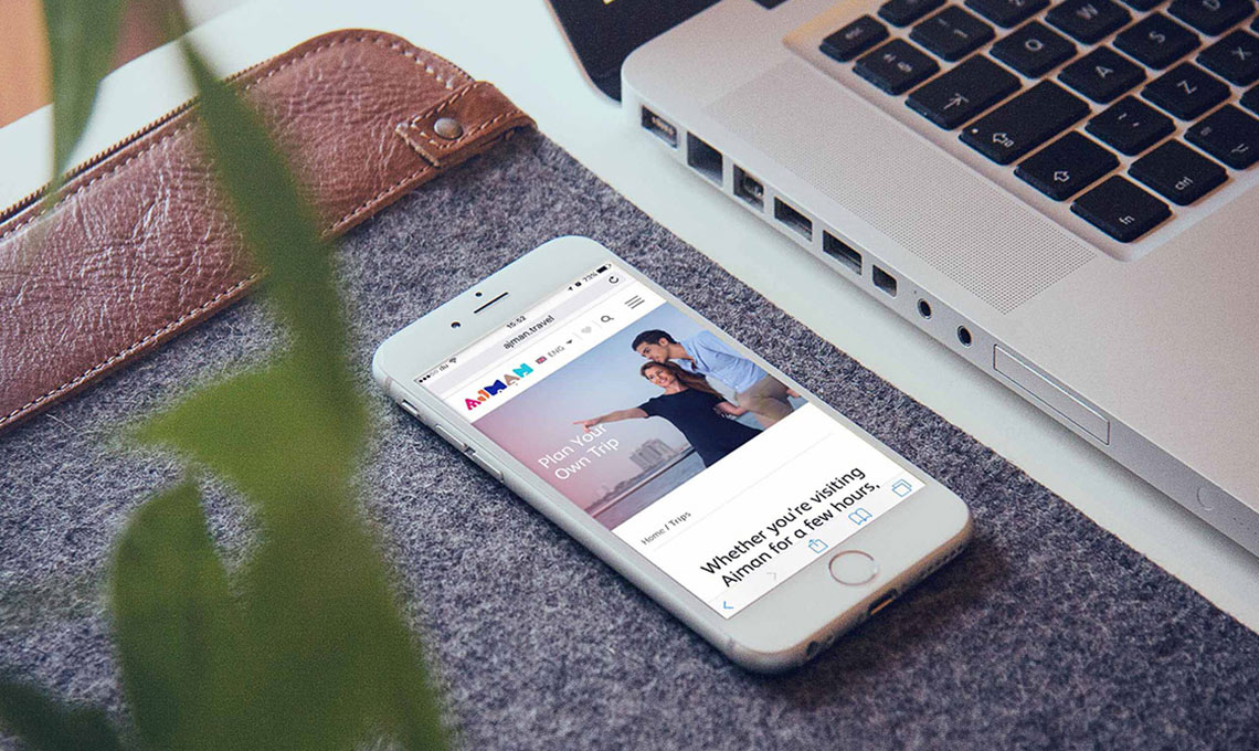 An iphone displaying a news article on a desk next to a laptop.