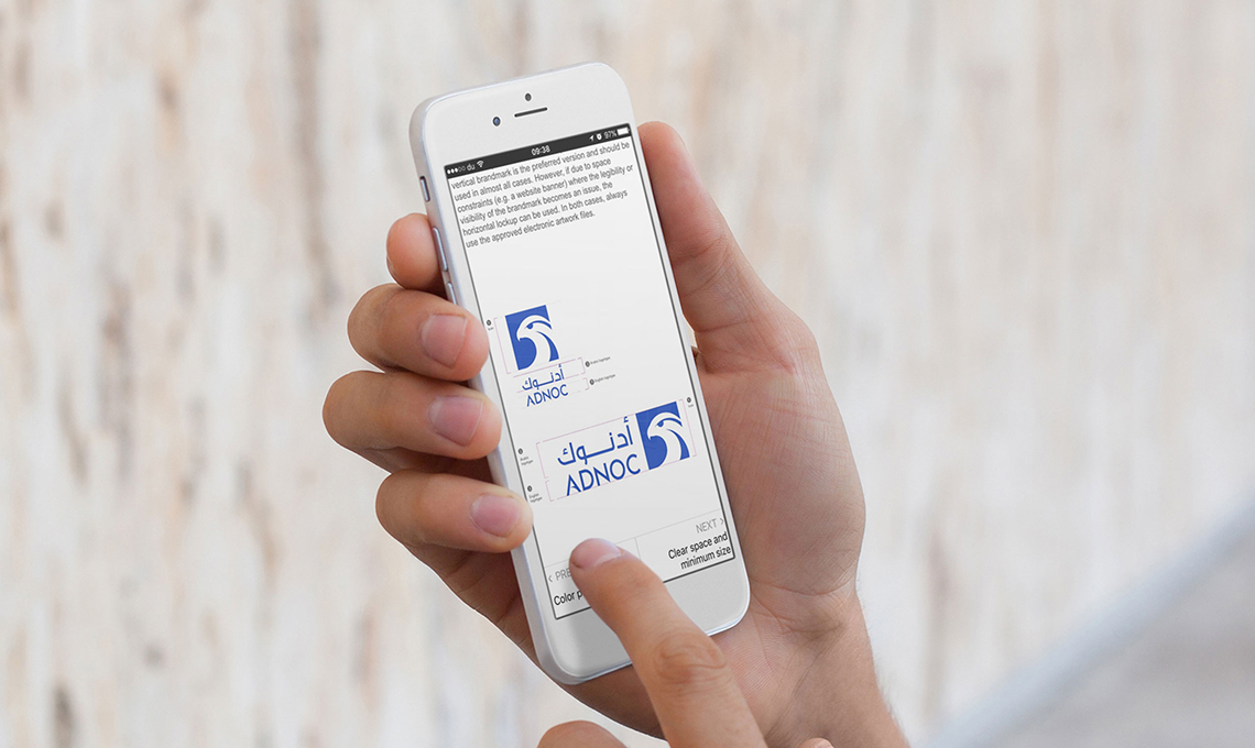 A man with a mobile phone in his hand with the brand management system designed and developed for ADNOC with BrandOS