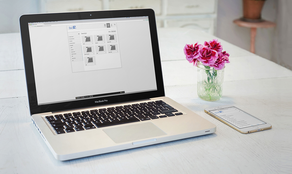 A laptop and a mobile phone on a desktop with the brand management system designed and developed for ADNOC with BrandOS