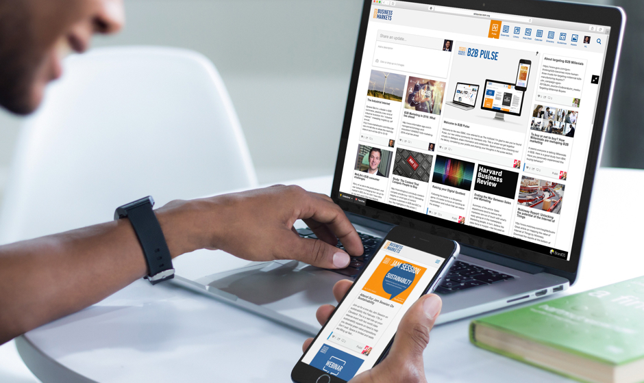 A man is using a laptop and a cell phone for BrandOS, the next-generation brand management software.