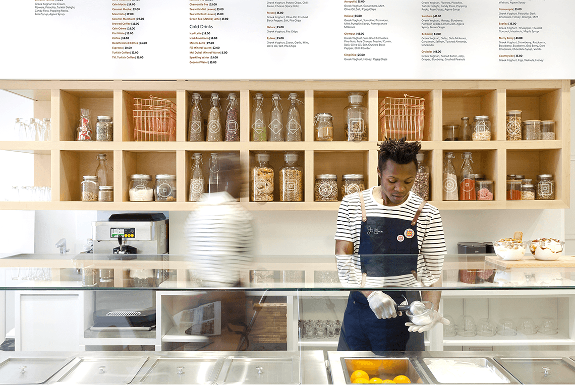 a woman standing in front of a counter serving yogurt