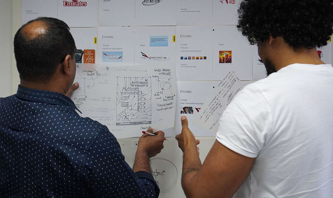 Two men standing in front of a wall with paper on it.