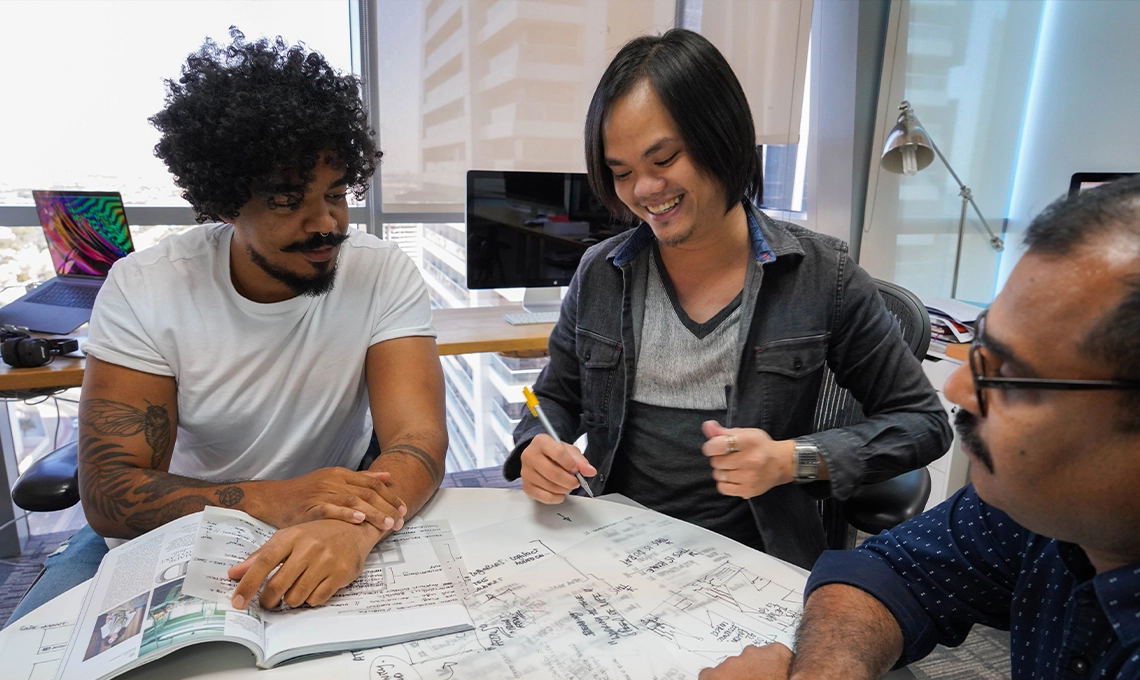 Three men sitting at a table reviewing designs