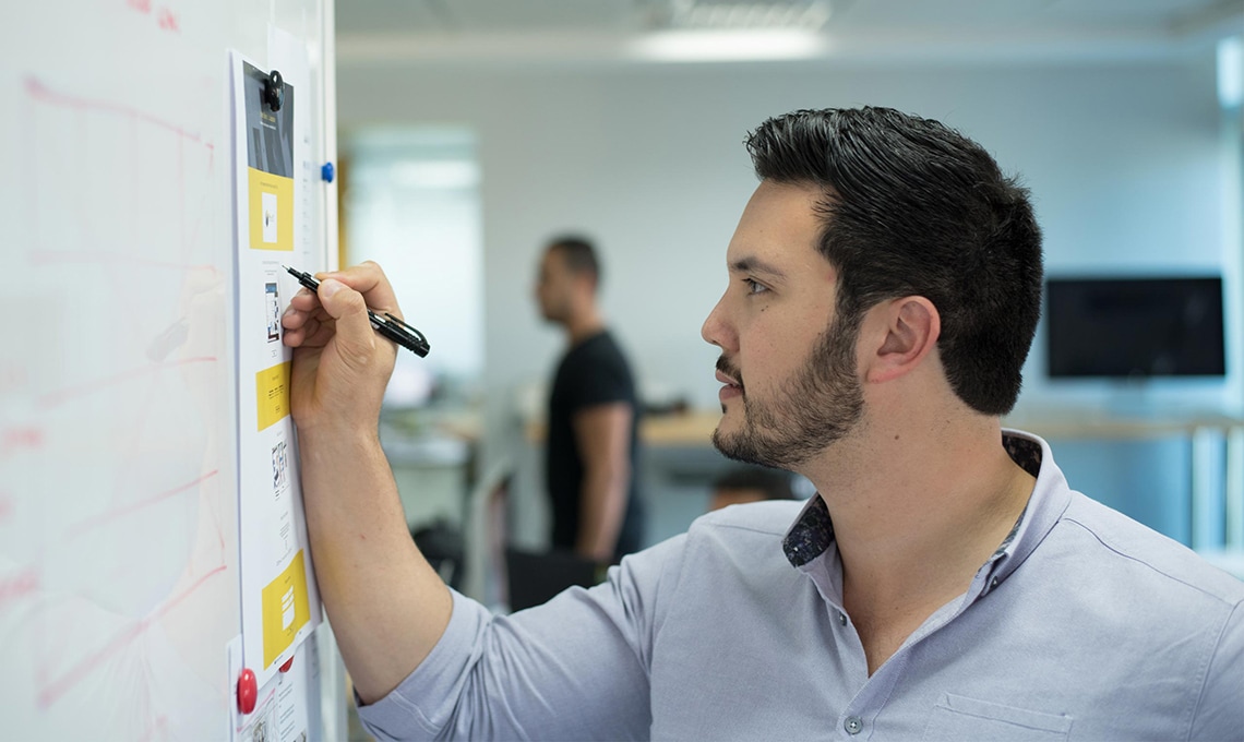 A man writing on a whiteboard in an office.