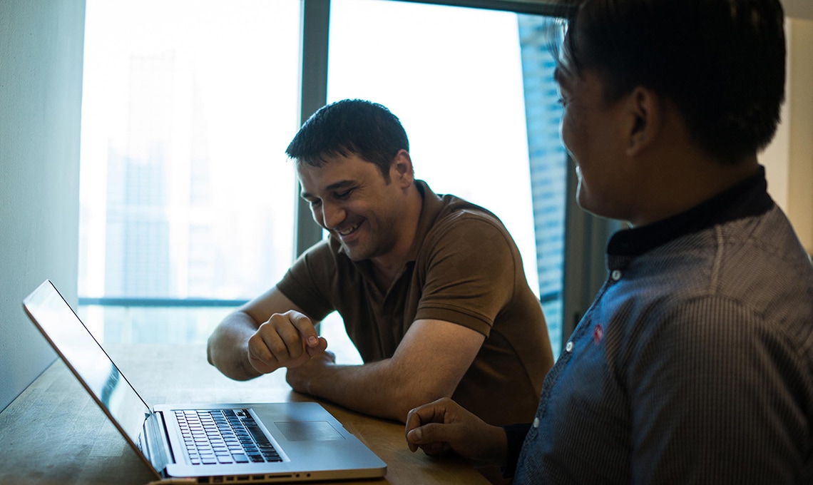 Two men sitting at a table looking at a laptop.