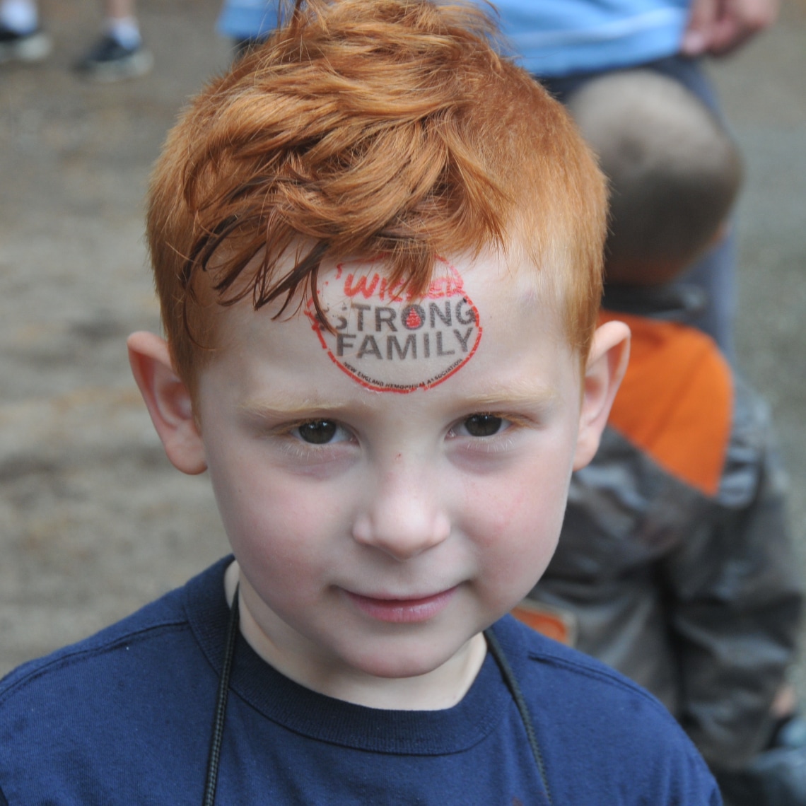 a young boy with a logo of NEHA on his forehead that says "strong family".