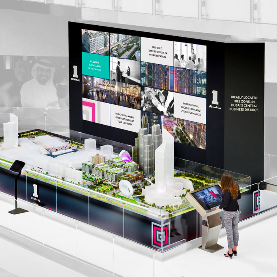 a woman looking at a model of a city and a multimedia wall developed for One Central.