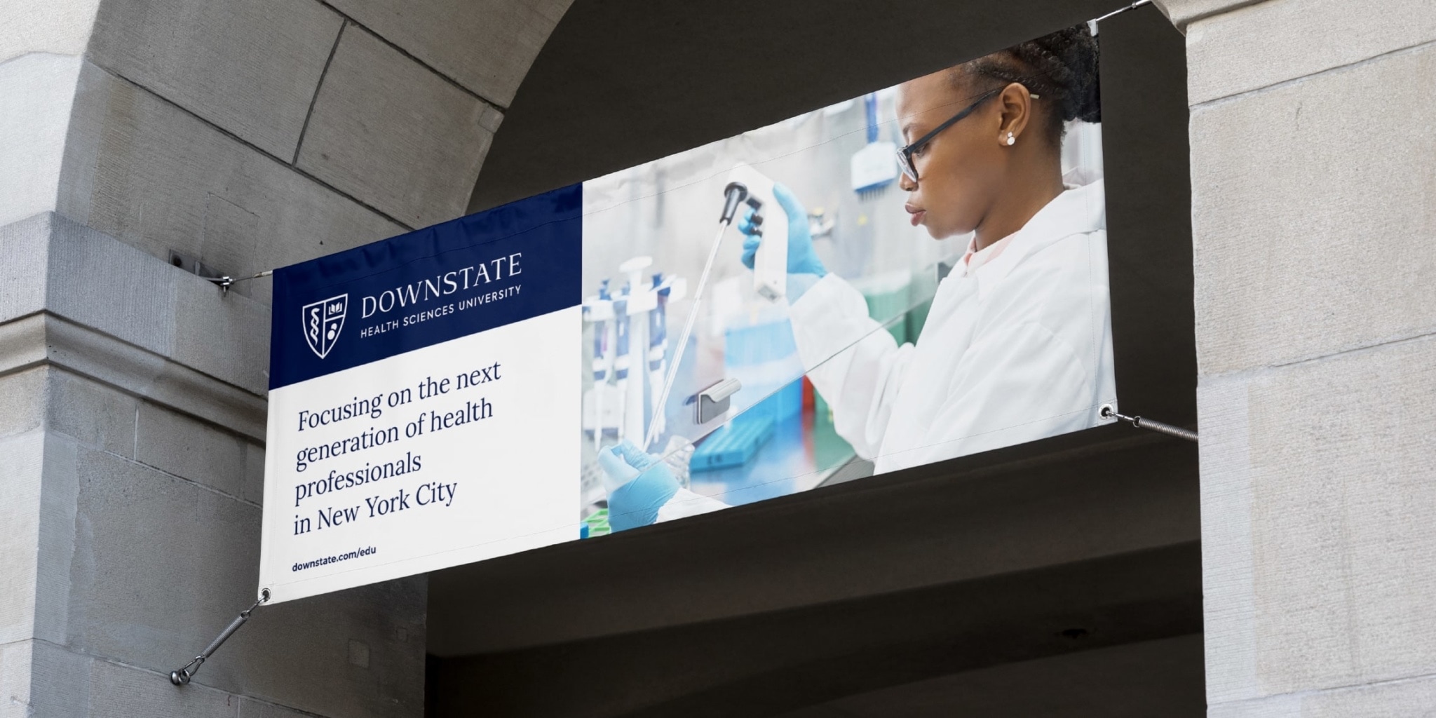 Example of a large horizontal banner showing how to apply the design system for SUNY hanged at the base of an arch