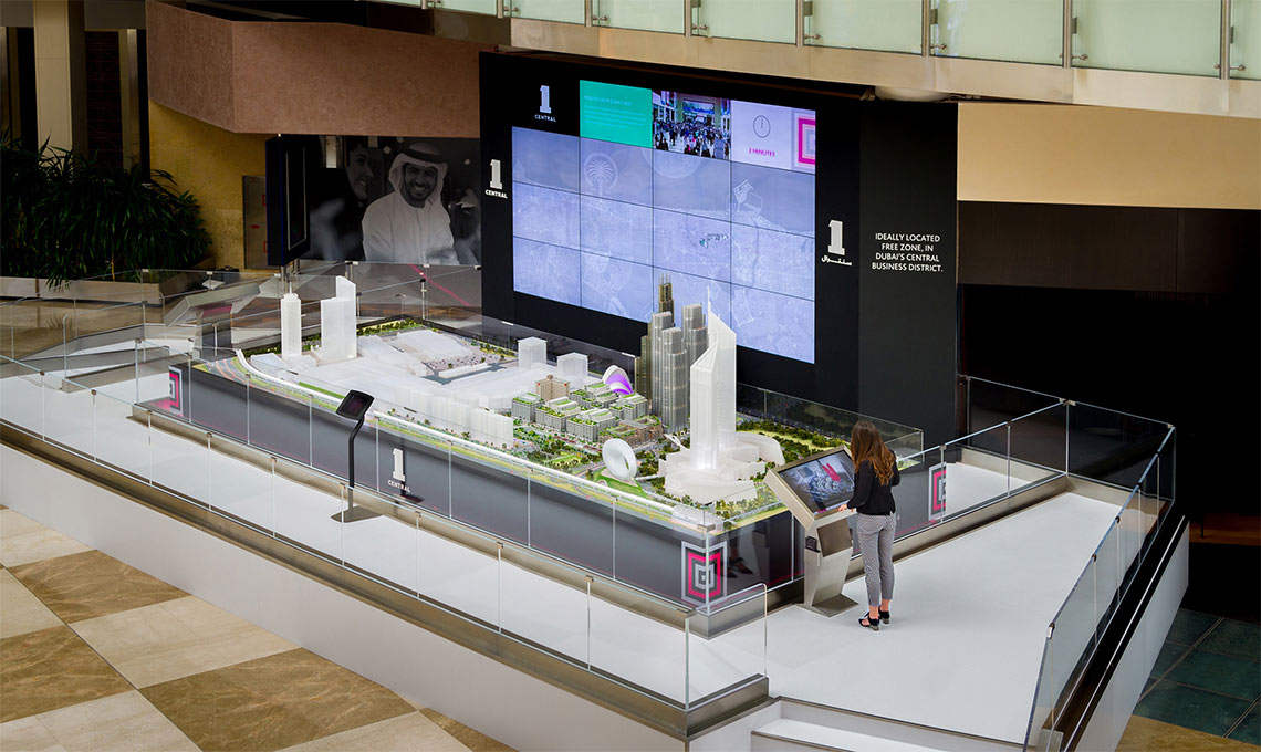 a woman looking at a model of a city in front a multimedia wall controlled by touchscreen devices