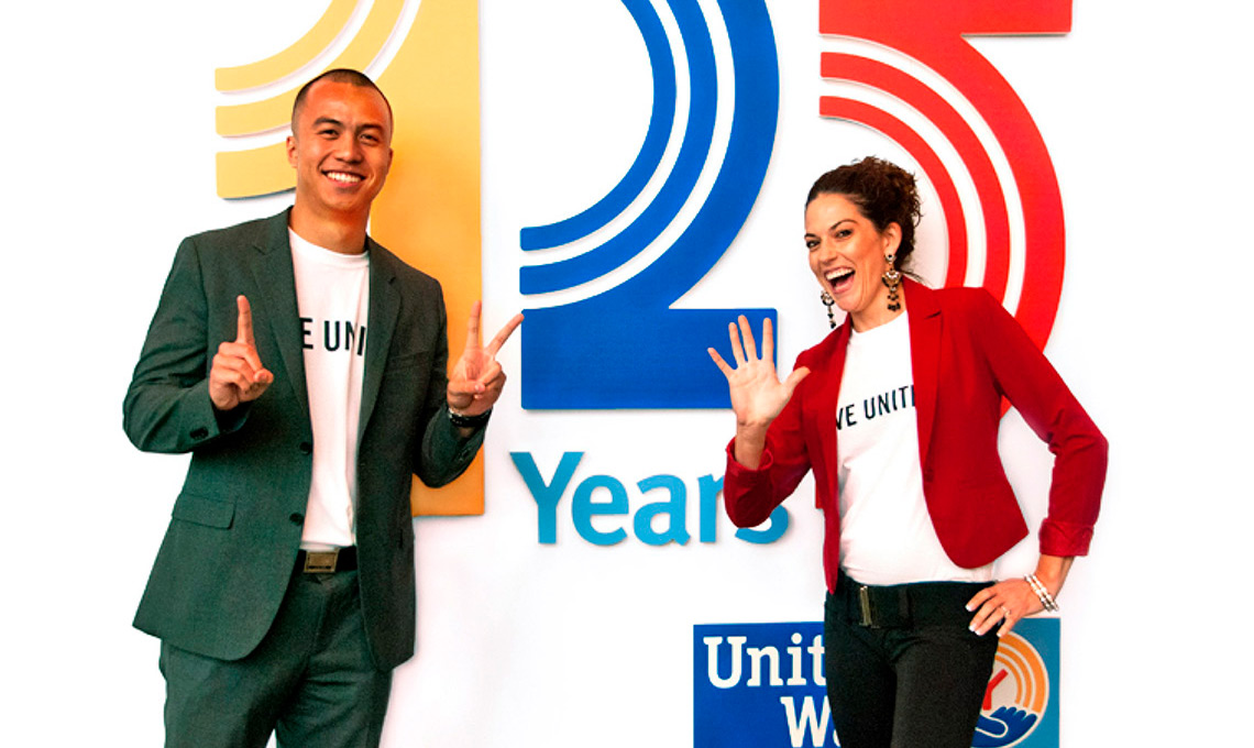 Two people posing in front of a sign that says 25 years.