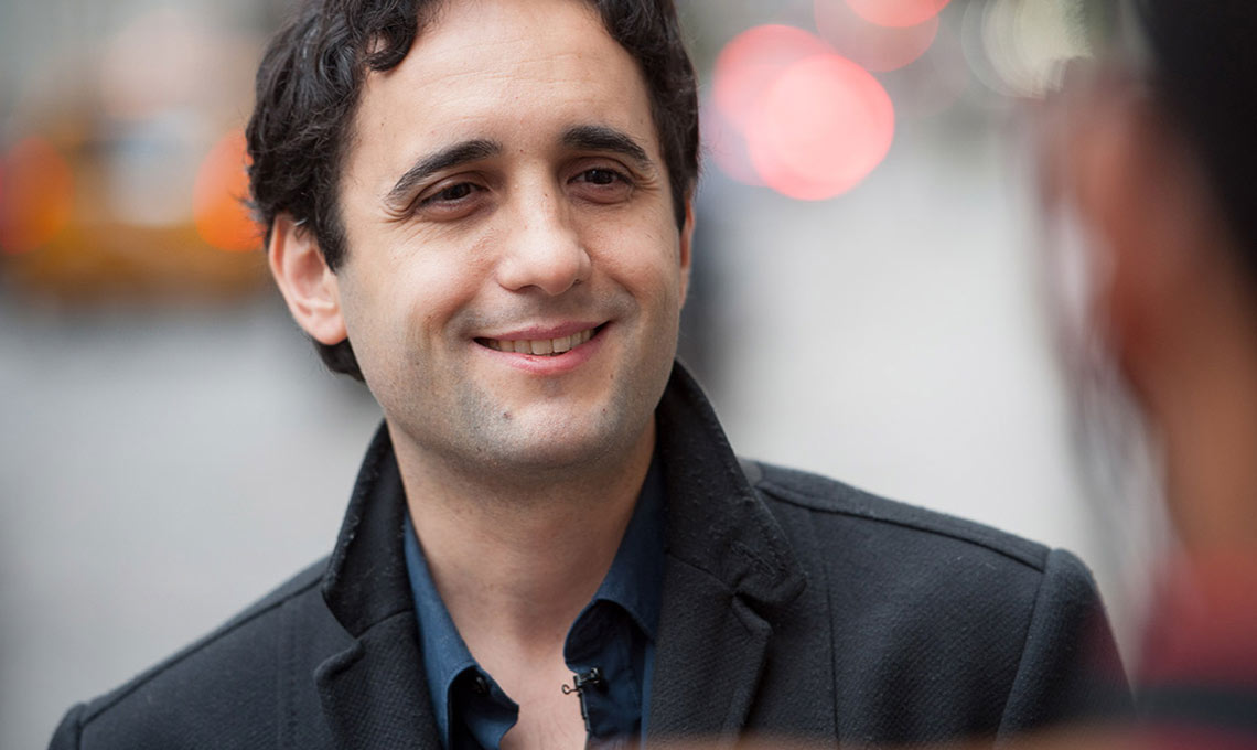 A smiling man in a black jacket and blue shirt showcasing a mobile app.