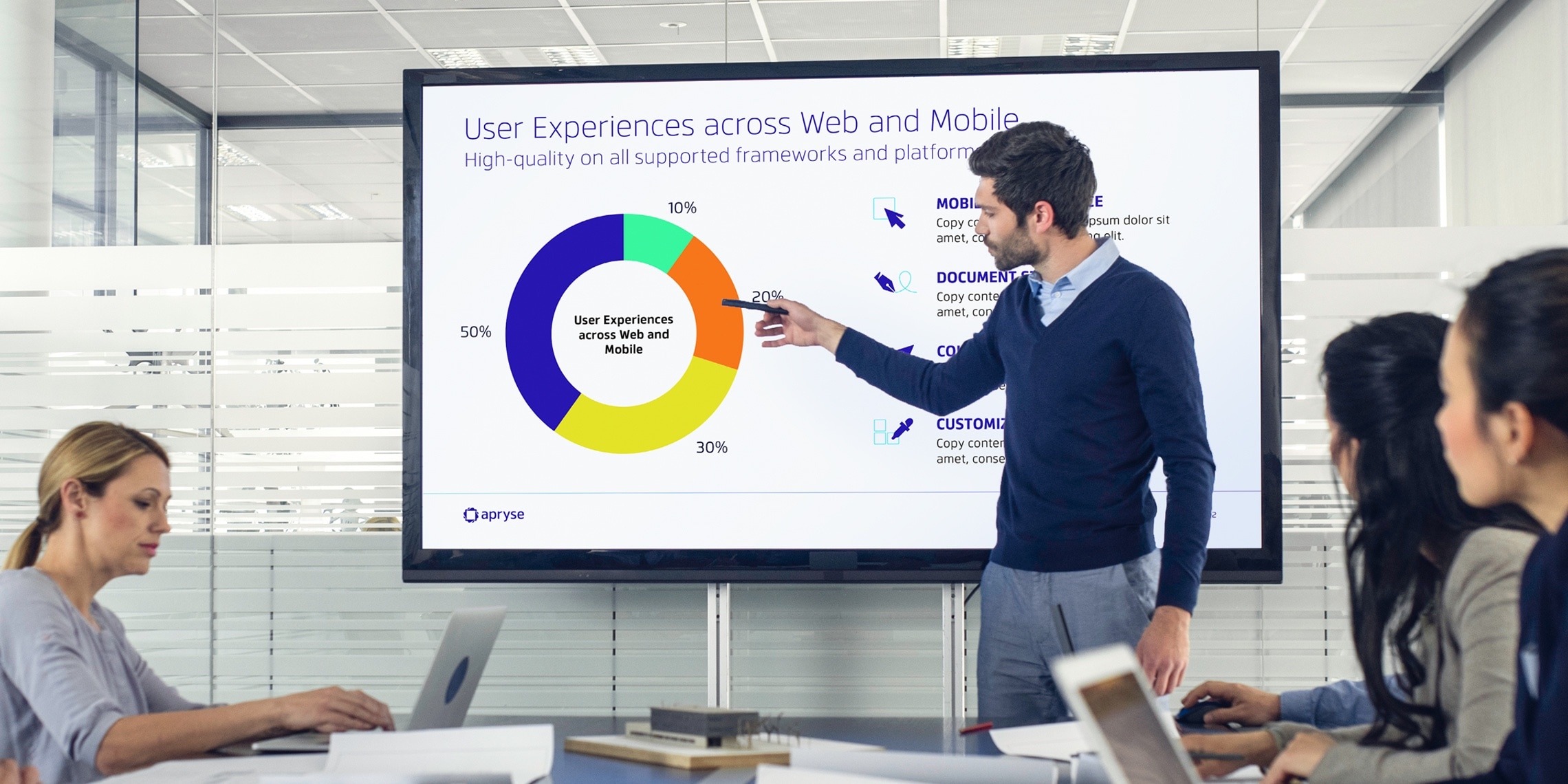 a group of employees in a meeting room watching a presentation on a large screen with the design system developed for Apryse