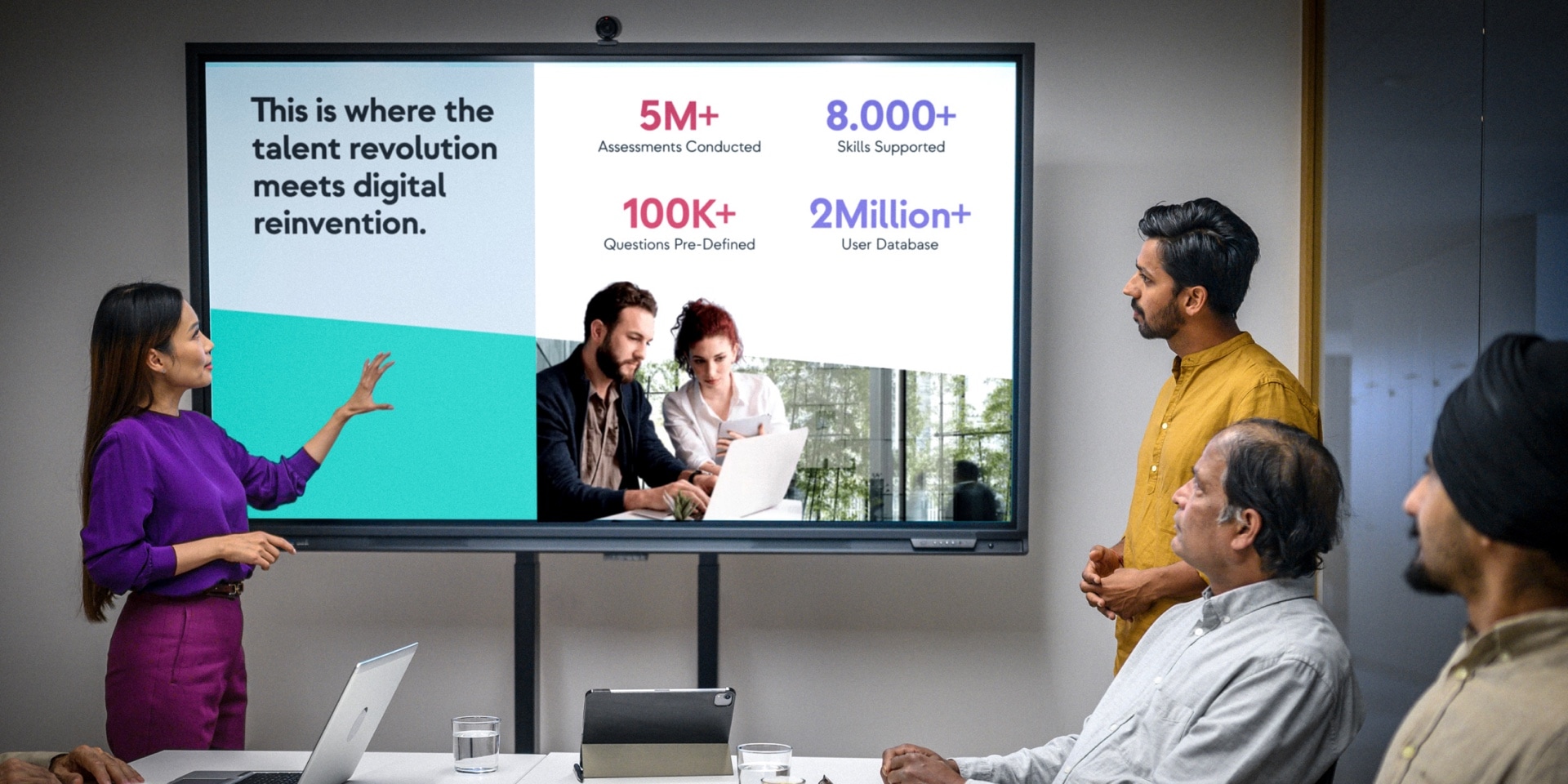A woman giving a presentation designed for Talent Titan on a large screen to a group of colleagues