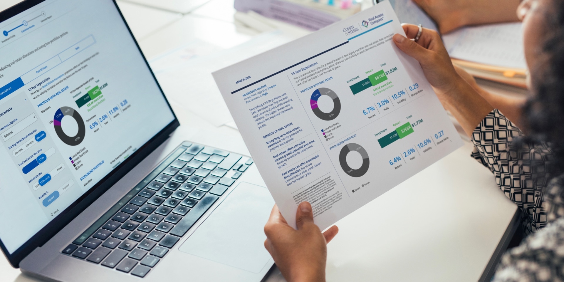 A woman holding a printed web page of the Real Asset Compass Tool displayed in a laptop