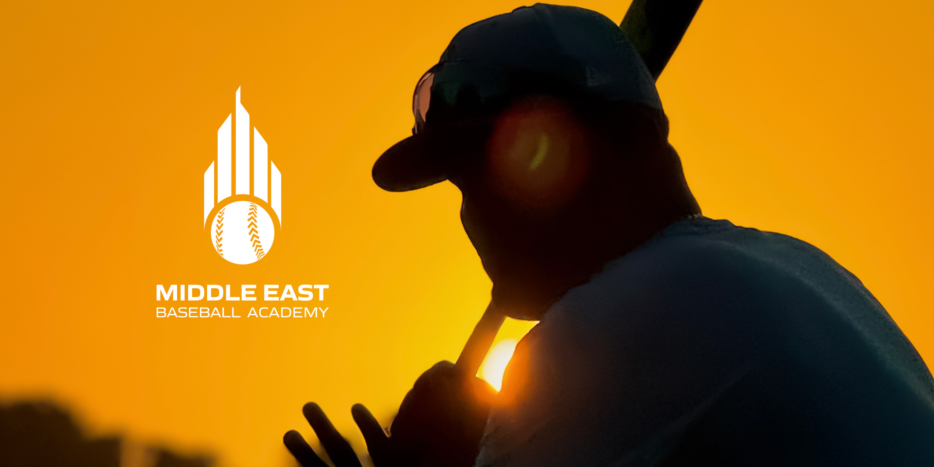 A professional baseball coache of the Middle East Baseball Academy holding a baseball bat during sunset.