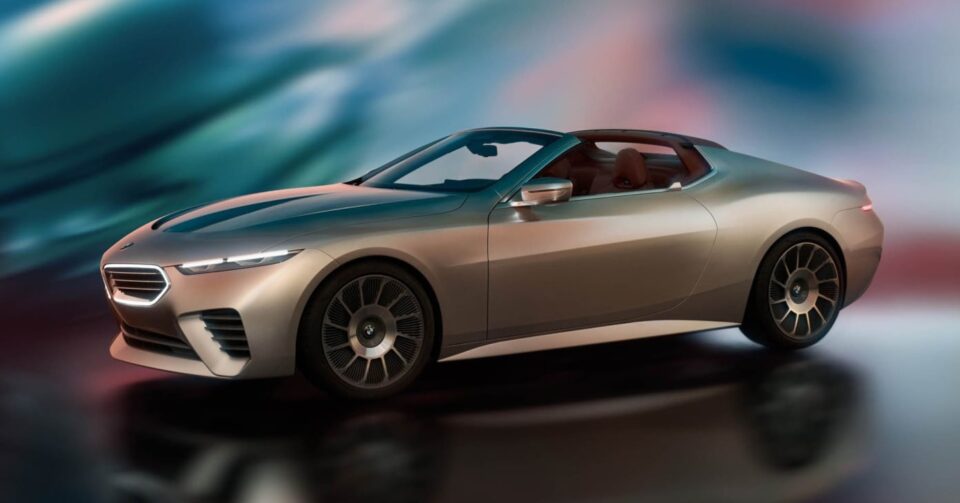 A silver, two-door sports car with a sleek design is parked on a reflective surface against a blurred, colorful background.