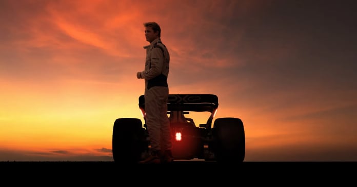 A person in a racing suit stands next to a formula-style race car at sunset, silhouetted against an orange sky.